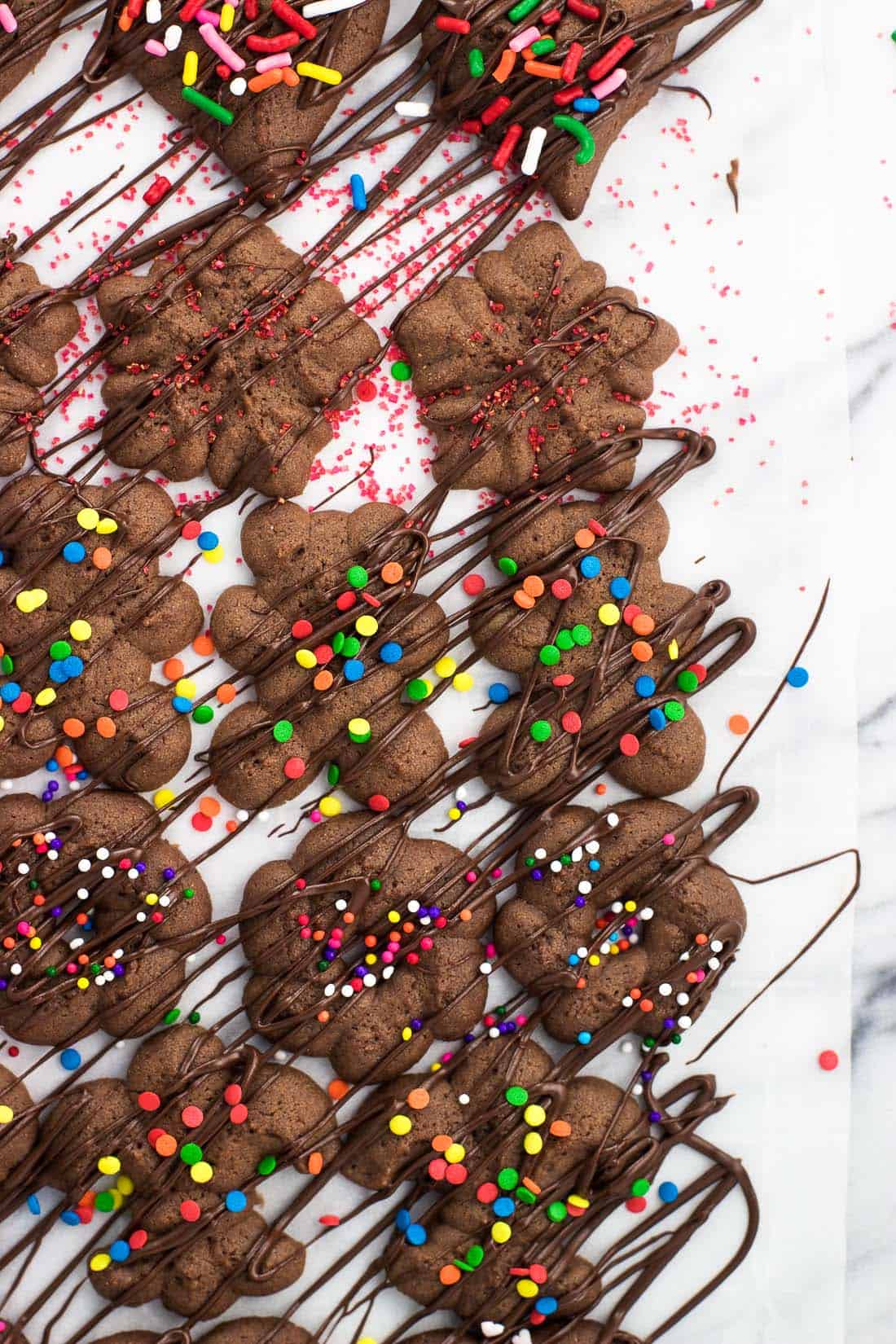 Cookies on a piece of parchment paper after being drizzled with melted chocolate and decorated with sprinkles.