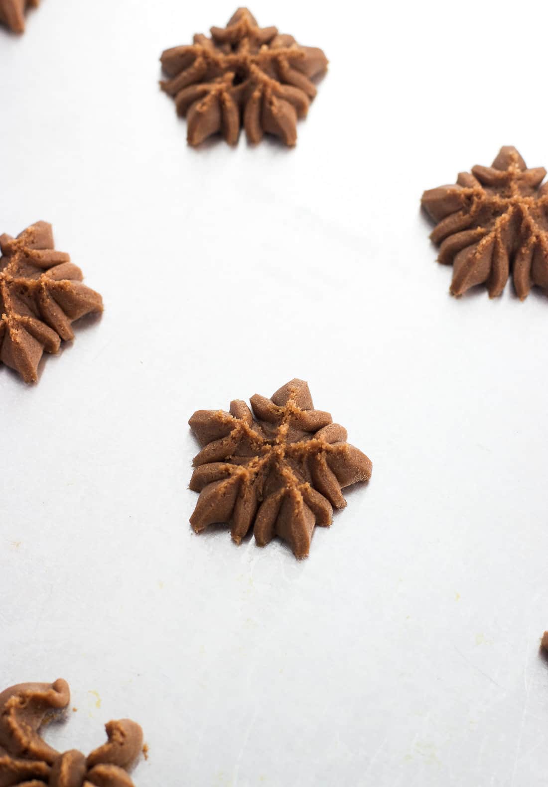 Spritz cookies shaped like a snowflake pressed onto a metal baking sheet before going in the oven.