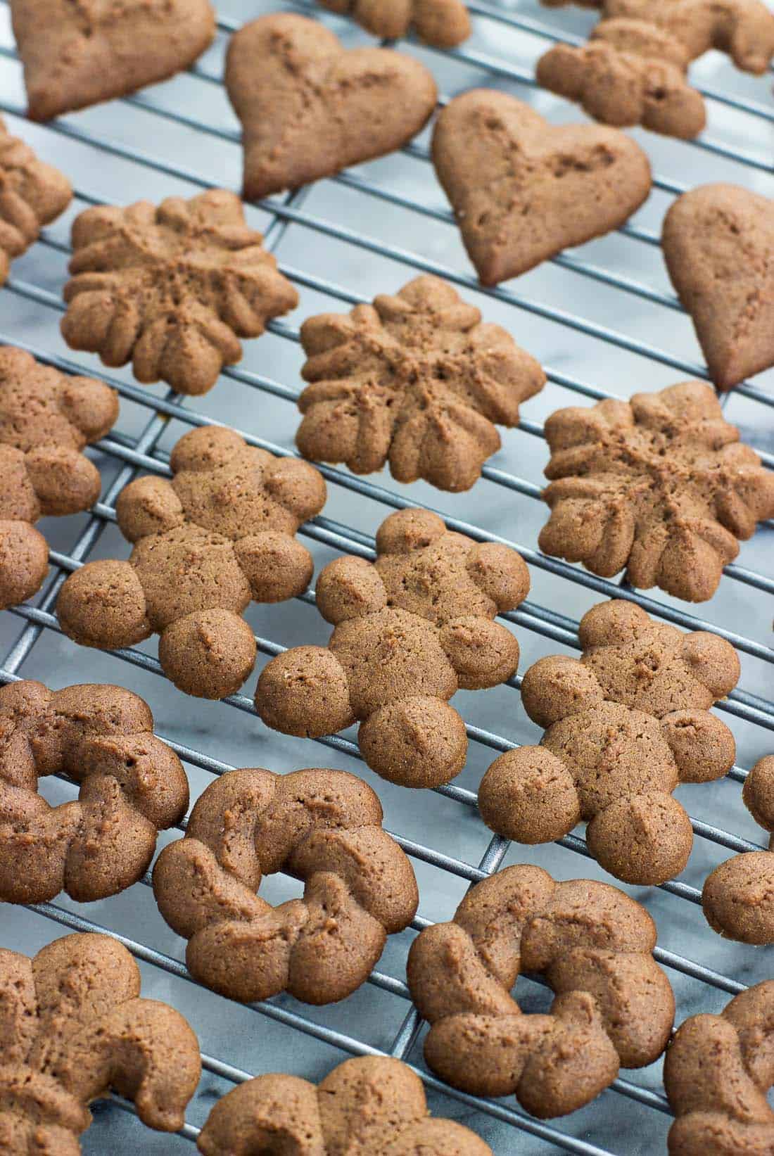 A close-up view of an assortment of shaped cookies on a rack, including a teddy bear shape, a wreath, a snowflake, and a heart.