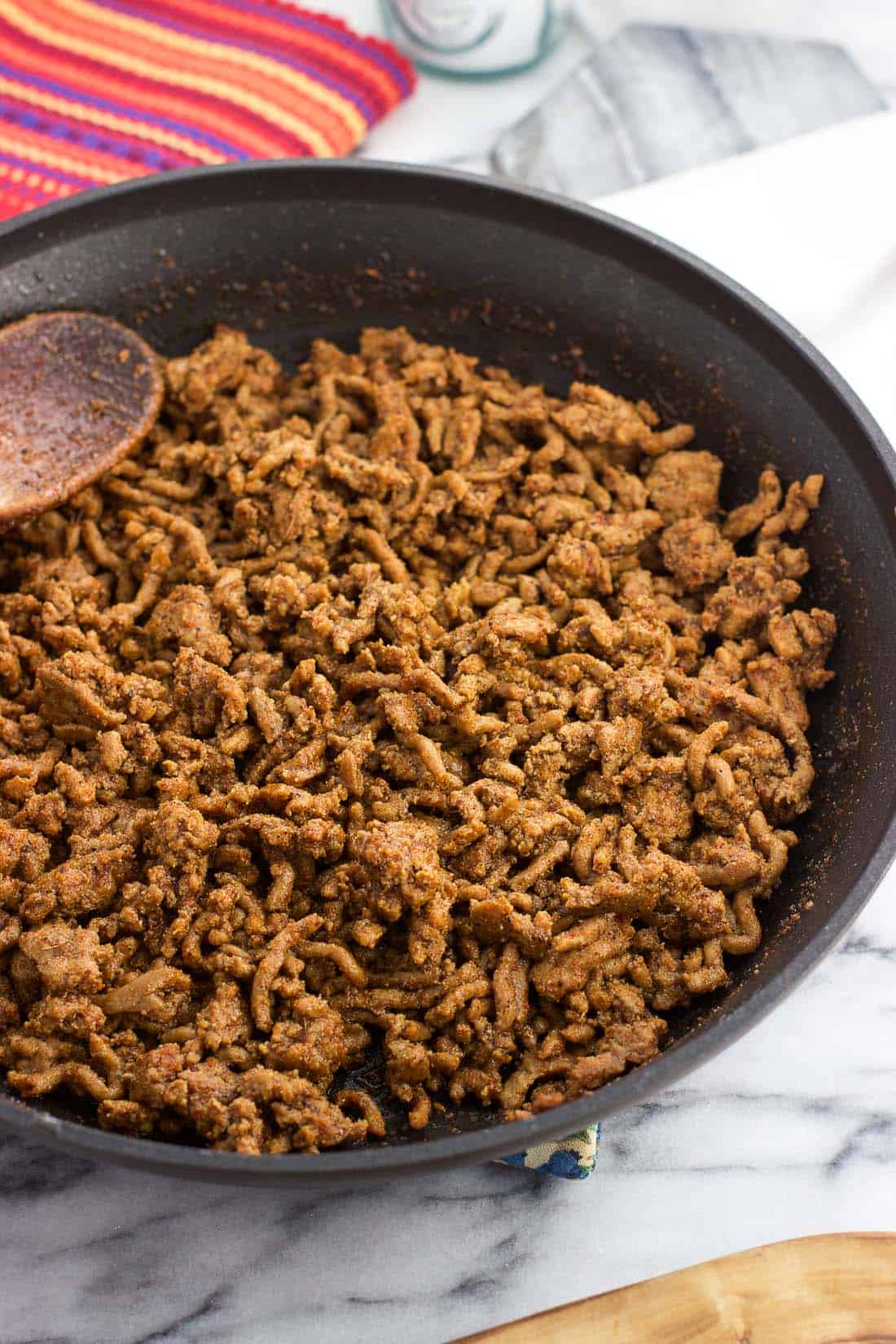 Cooked taco meat in a skillet with a wooden spoon.
