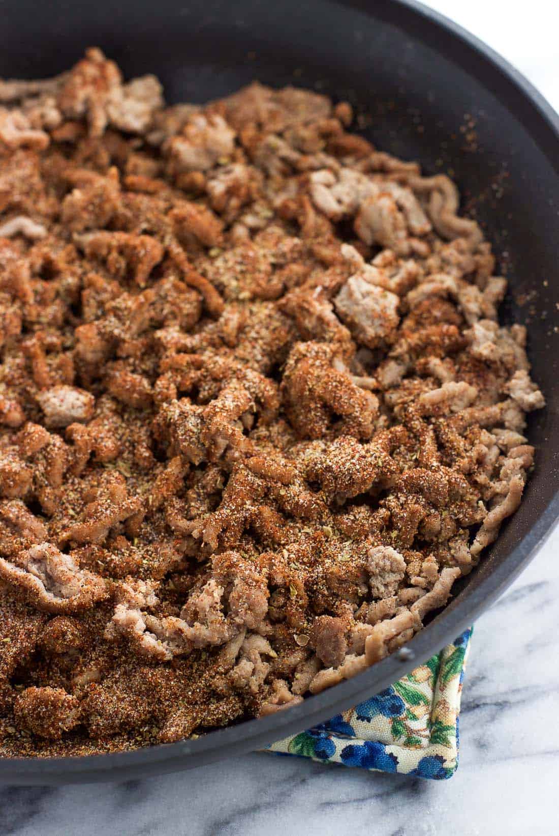 Taco seasoning sprinkled over cooked and crumbled ground beef in a skillet.