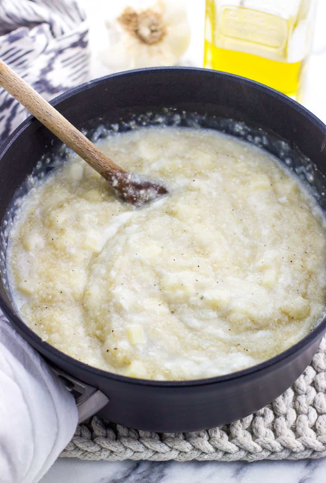 Cheese and milk being stirred into the cooked grits by a wooden spoon in a saucepan