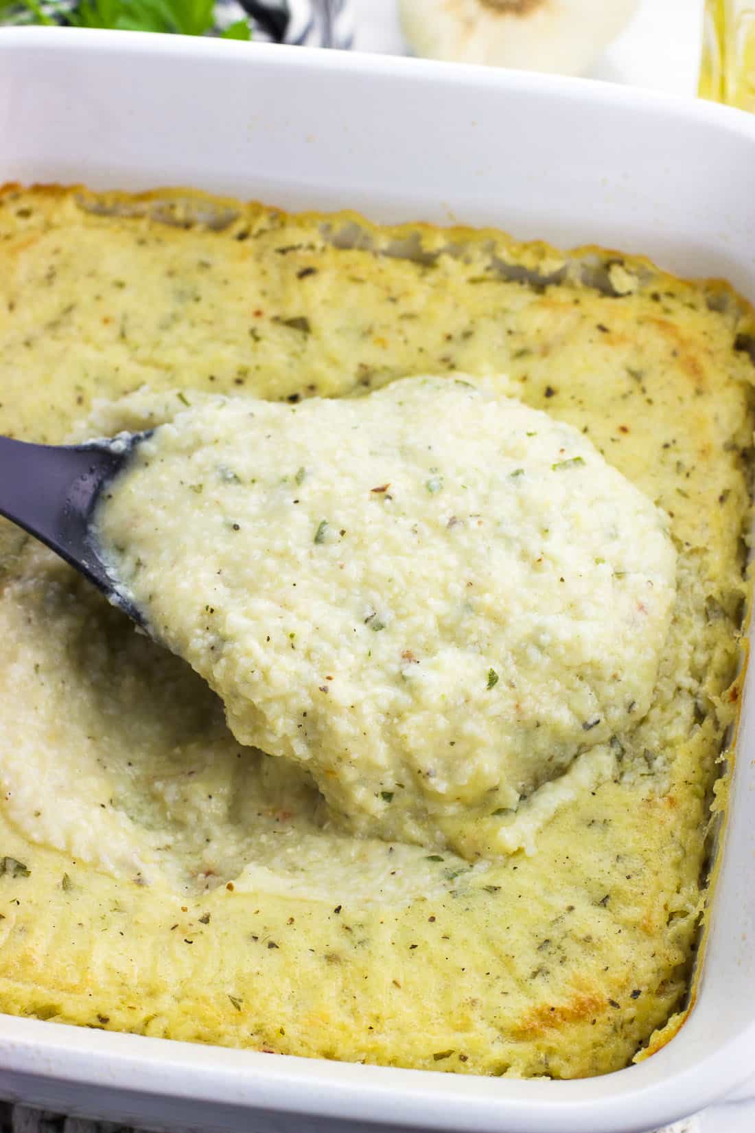 A big serving spoon of baked grits being lifted out of the baking dish