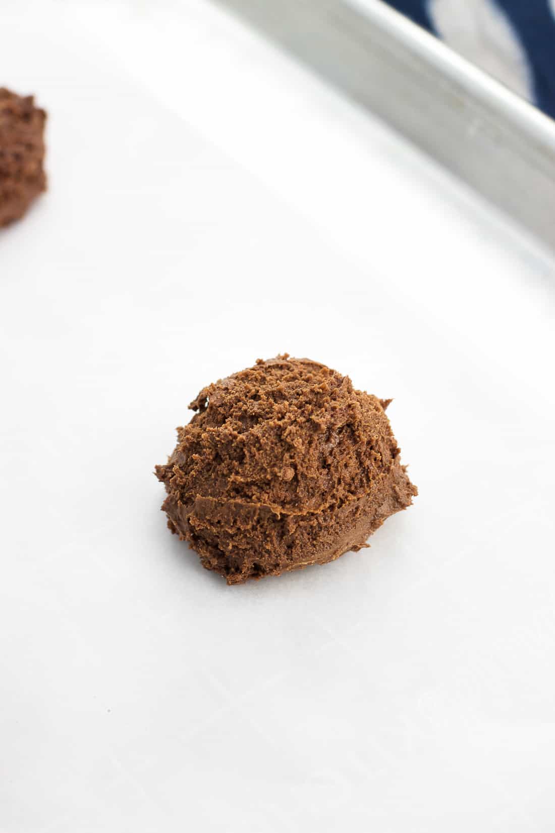 A rounded scoop of brownie cookie batter on a parchment-lined baking sheet