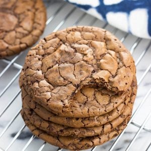 A stack of five brownie cookies on a wire rack with a bite taken out of the top one