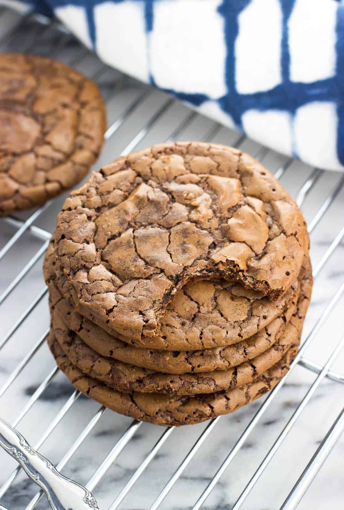 A stack of five brownie cookies on a wire rack with a bite taken out of the top one