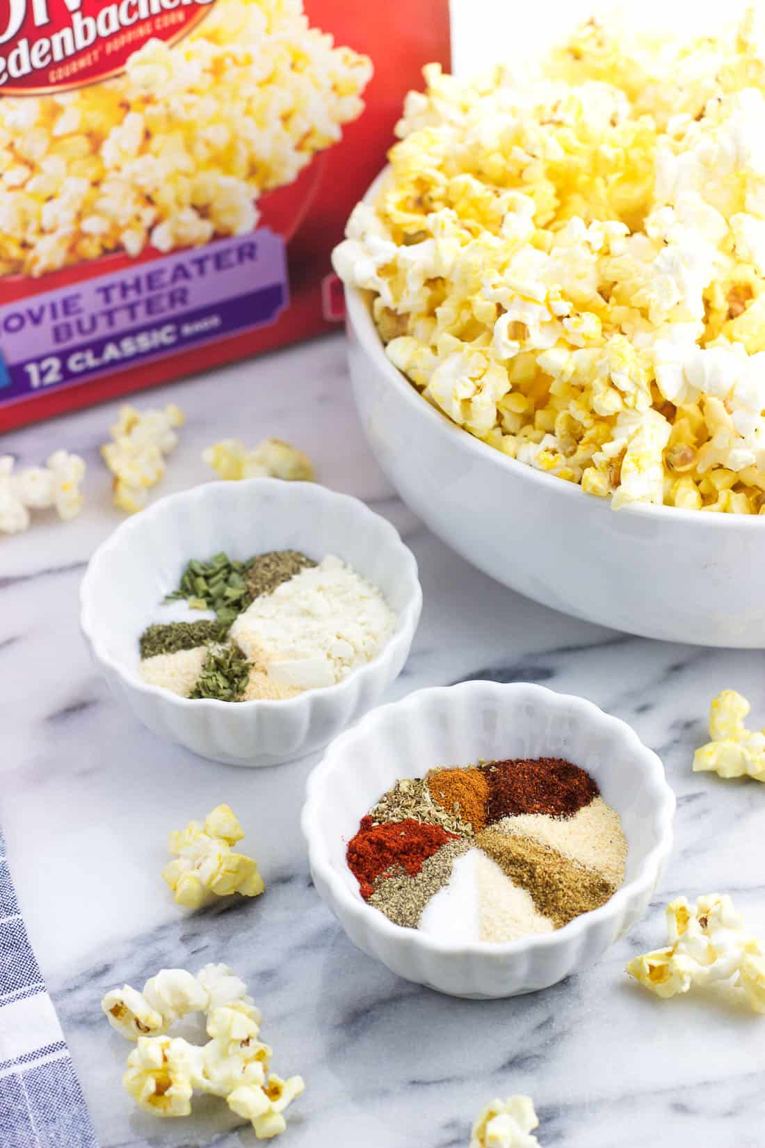 Two small bowls filled with spice mixes next to a large bowl of popped butter popcorn