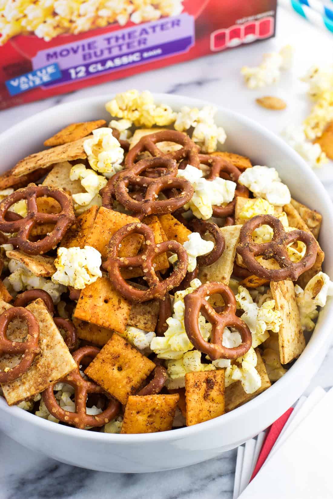 A bowl of popcorn snack mix next to a stack of napkins and paper straws for serving at a party