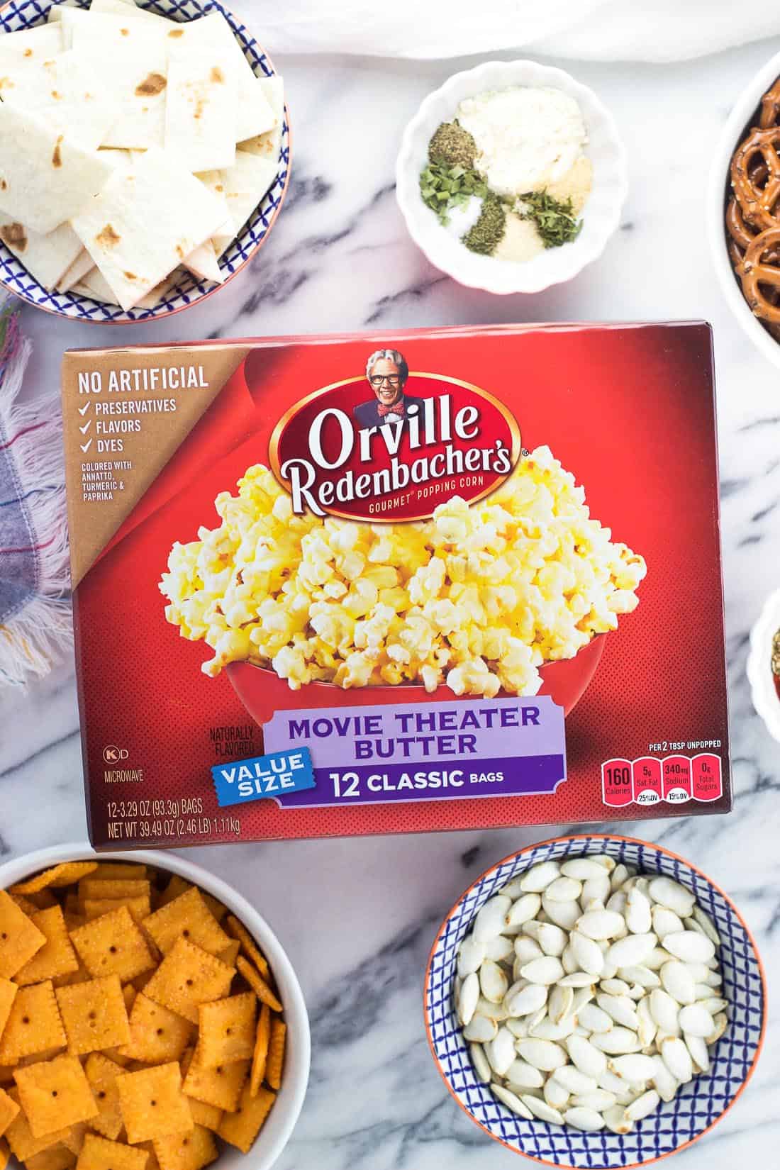 A box of popcorn on a marble board surrounded by the recipe ingredients in separate bowls