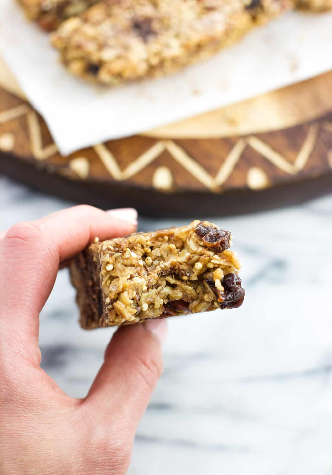 A hand holding a granola bar with the rest of them on a board in the background