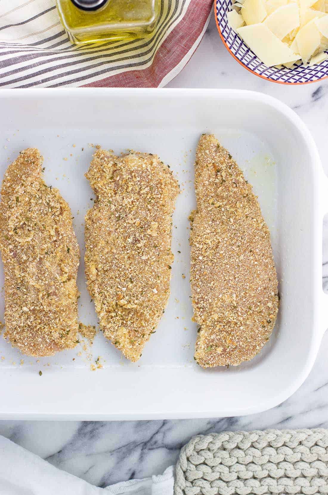 Chicken cutlets coated in breadcrumbs in a single layer in a large rectangular baking dish.