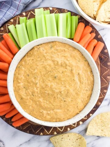 An overhead shot of buffalo dip in a serving bowl surrounded by baby carrots, celery sticks, and tortilla chips