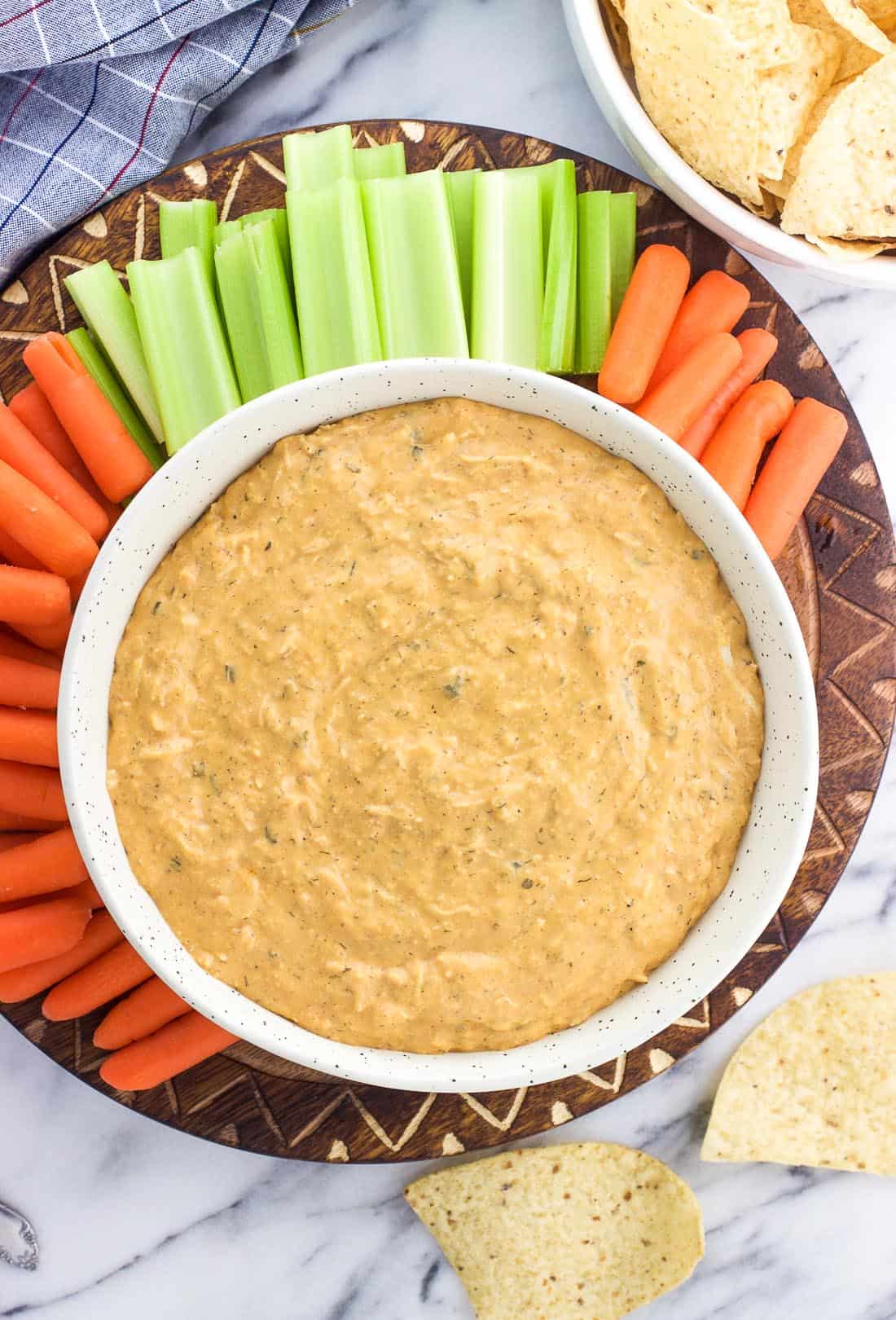 Buffalo dip in a serving bowl surrounded by baby carrots, celery sticks, and tortilla chips.