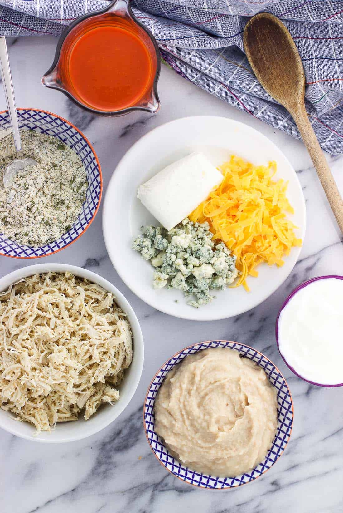 Buffalo dip ingredients in separate bowls and plates on a marble board.