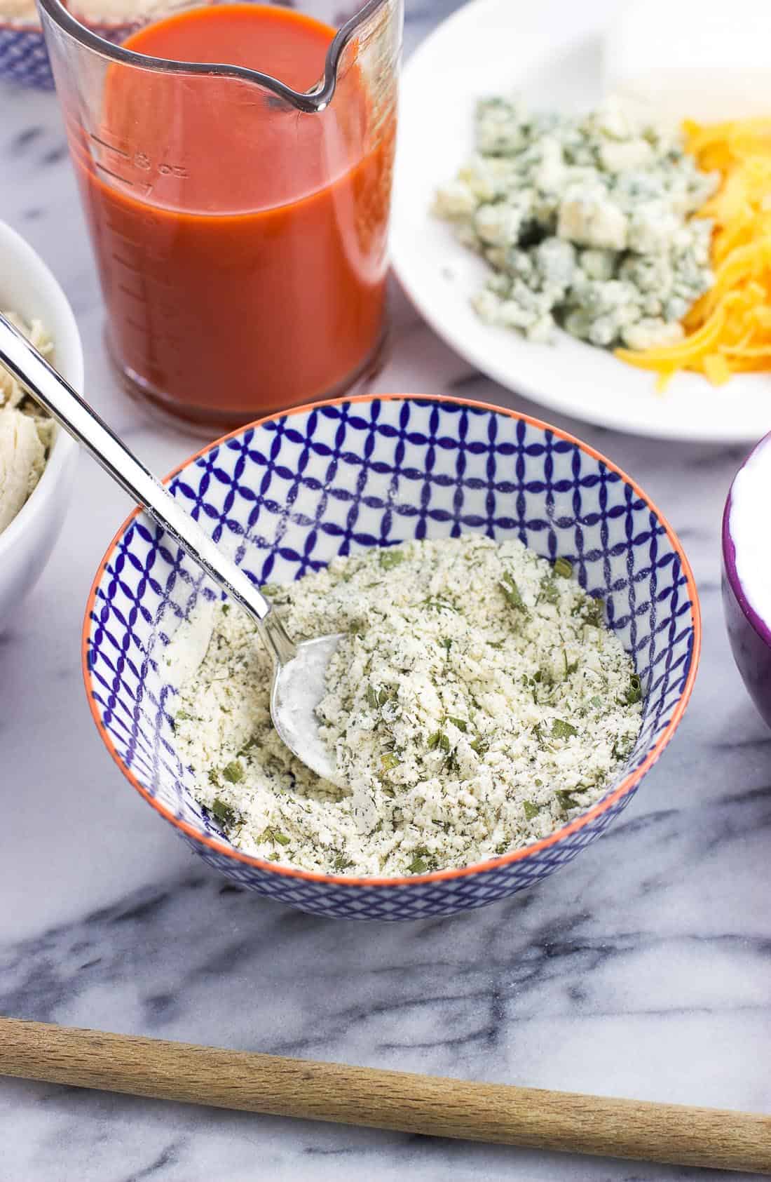 Homemade ranch seasoning in a small bowl with a spoon surrounded by other dip ingredients.