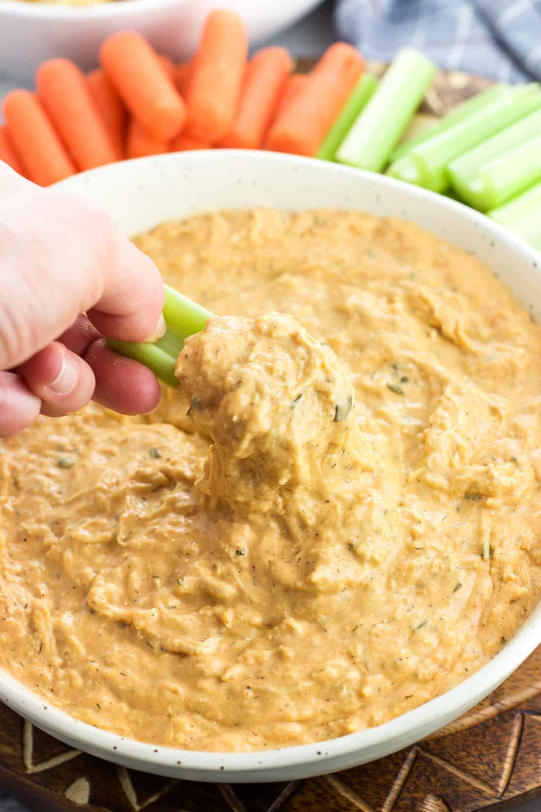 A hand scooping buffalo chicken dip with a celery stick.