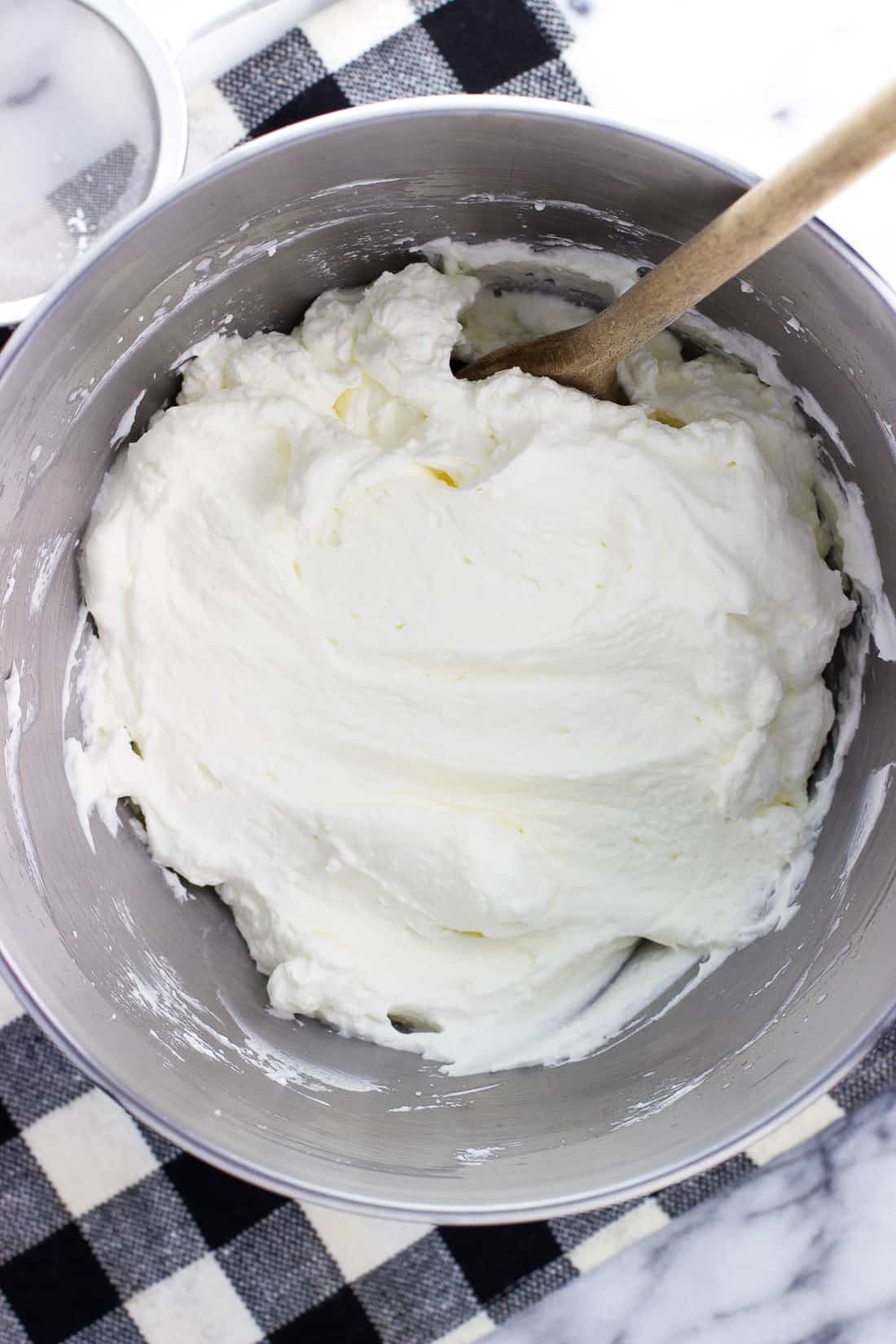 A stand mixer bowl of stabilized whipped cream with a wooden spoon.