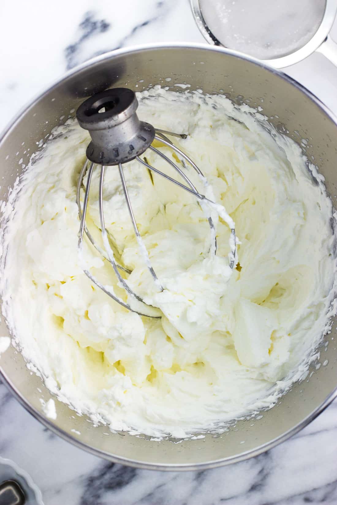 A metal stand mixer bowl of whipped cream with the beater attachment in it.