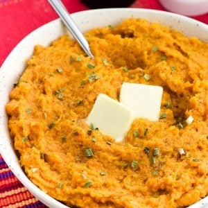 A bowl of mashed sweet potatoes topped with herbs and two pats of butter