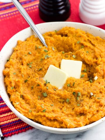 A bowl of mashed sweet potatoes topped with herbs and two pats of butter