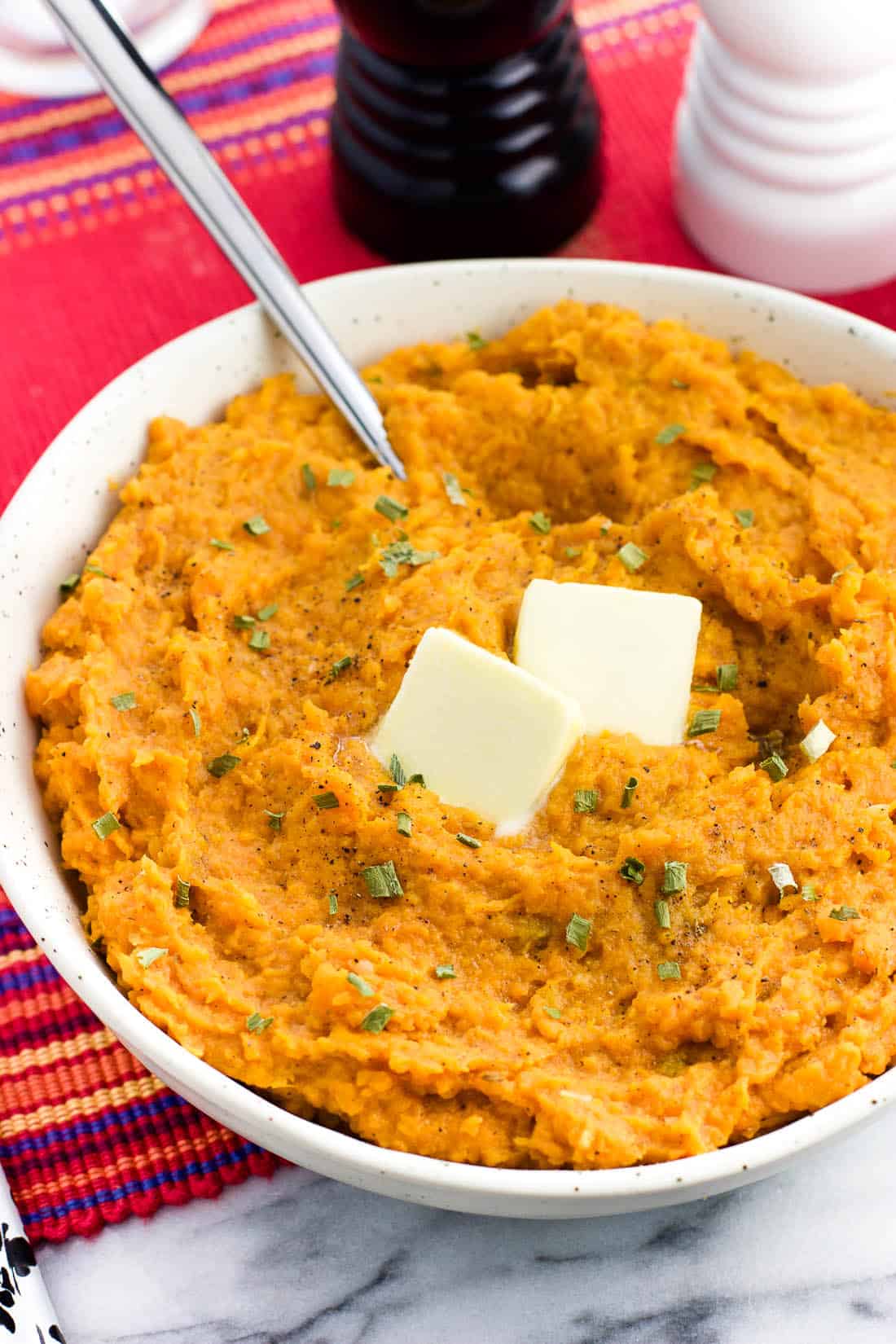 A bowl of mashed sweet potatoes topped with herbs and two pats of butter