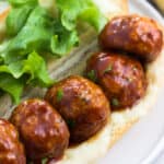Five BBQ glazed baked chicken meatballs open-face on a sub roll with melted cheese and lettuce