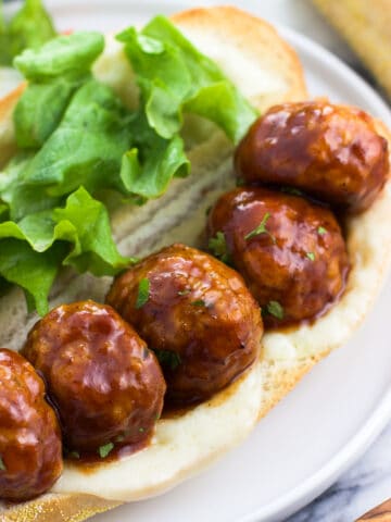 Five BBQ glazed baked chicken meatballs open-face on a sub roll with melted cheese and lettuce