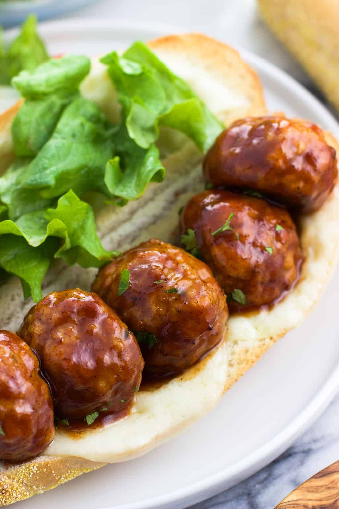 Five BBQ chicken meatballs open-face on a sub roll with melted cheese and lettuce.
