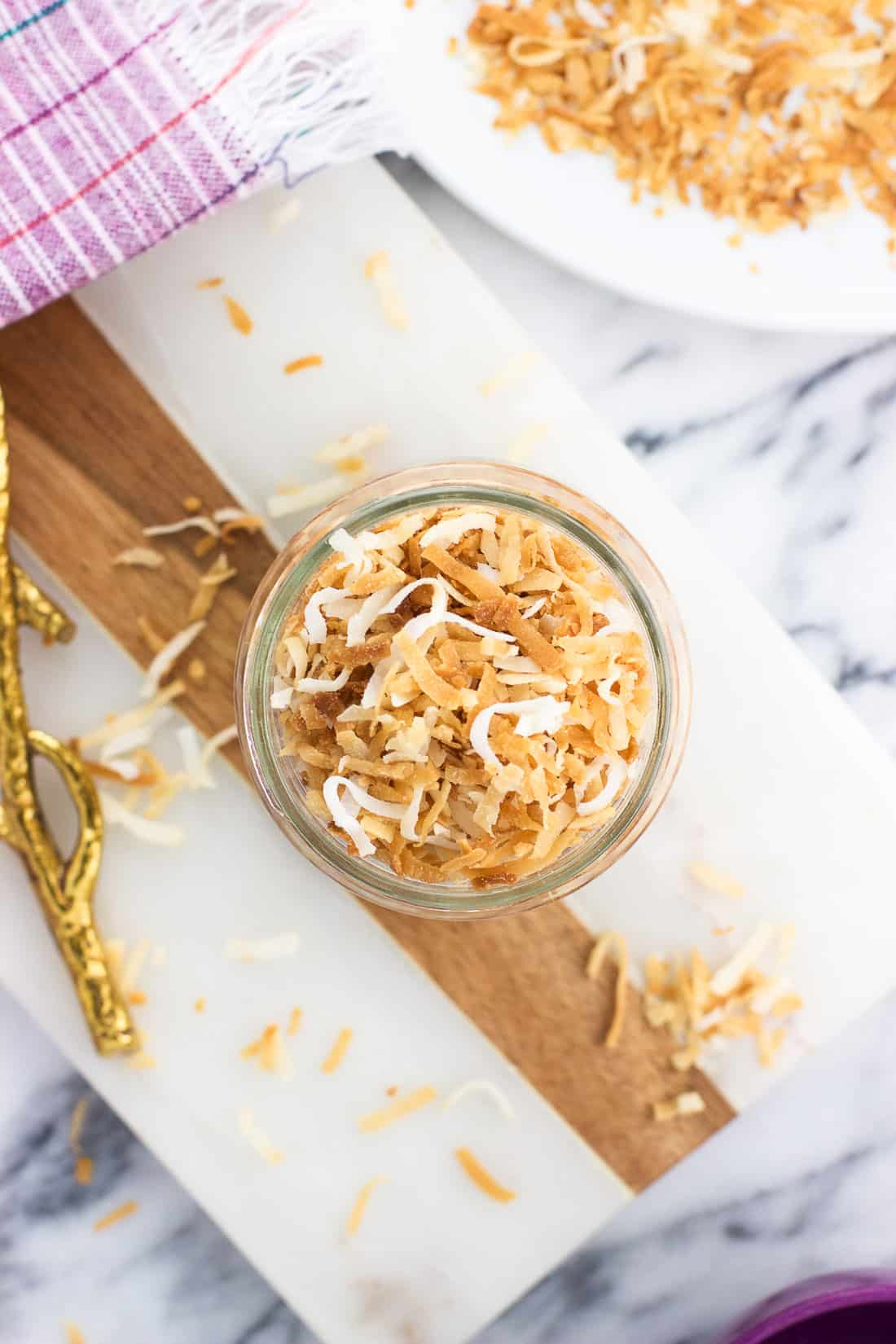 An overhead shot of toasted coconut in a jar, on a board, and a plate