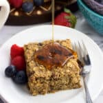 Fresh fruit and a baked oatmeal square on a plate being drizzled by maple syrup.