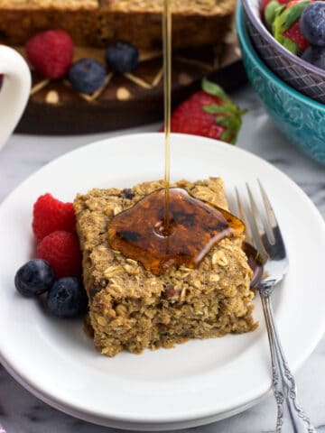 Fresh fruit and a baked oatmeal square on a plate being drizzled by maple syrup.