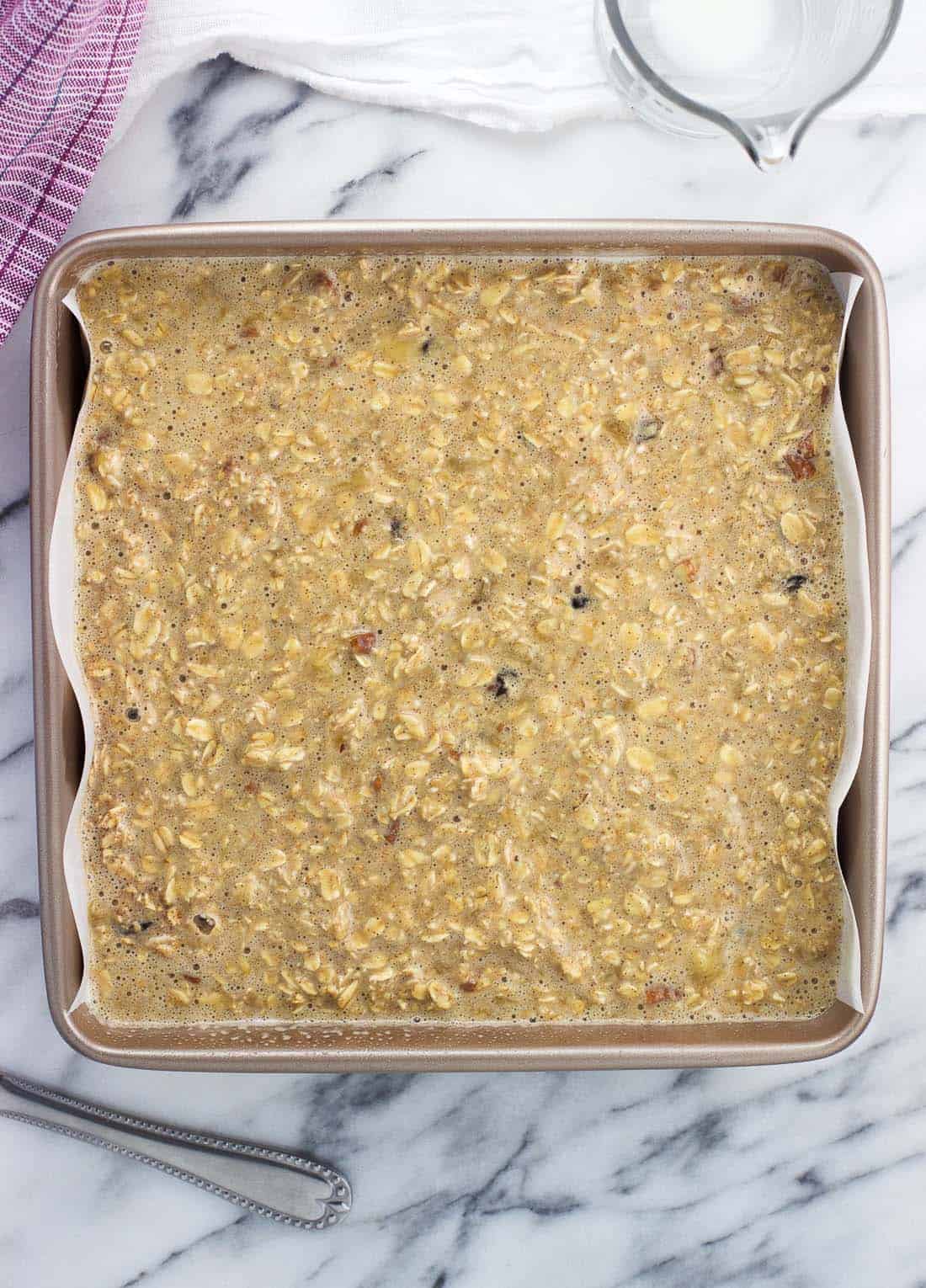 Oatmeal batter in a parchment-lined square pan.