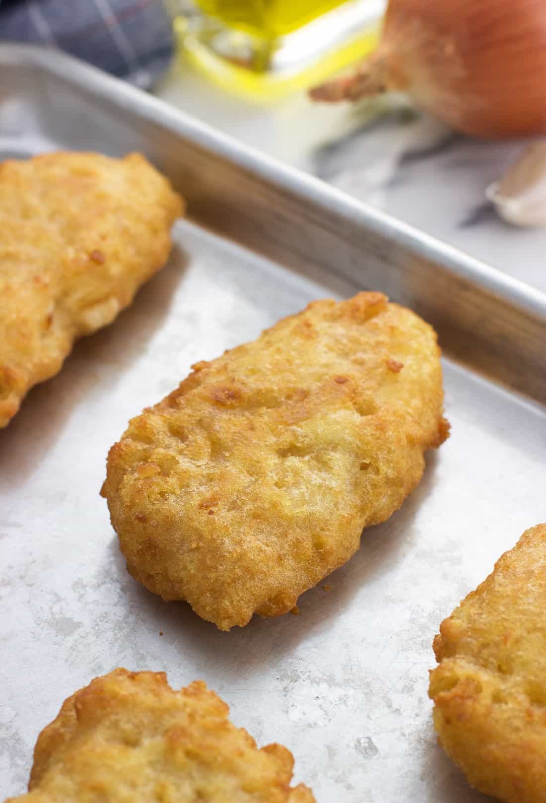 A close-up picture of a cooked beer battered cod fillet on a metal rimmed baking sheet.