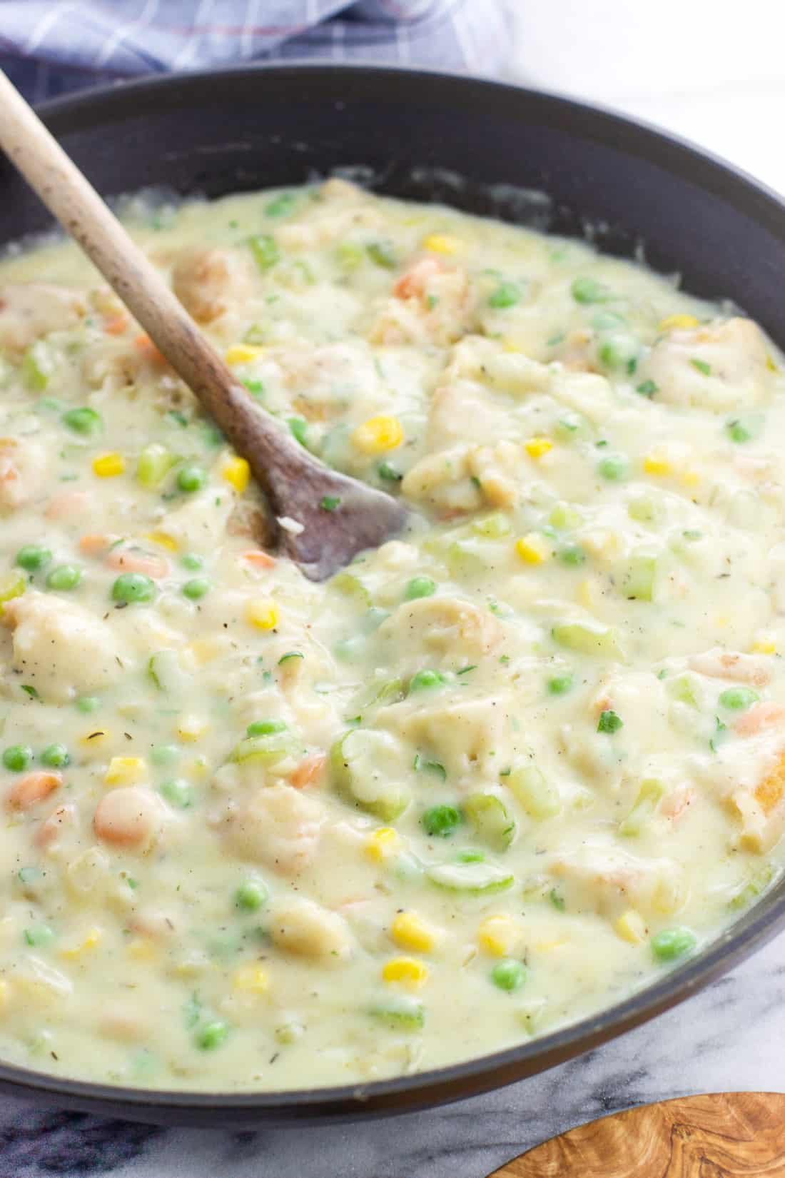 A thick and creamy pot pie mixture in a skillet with a wooden spoon.