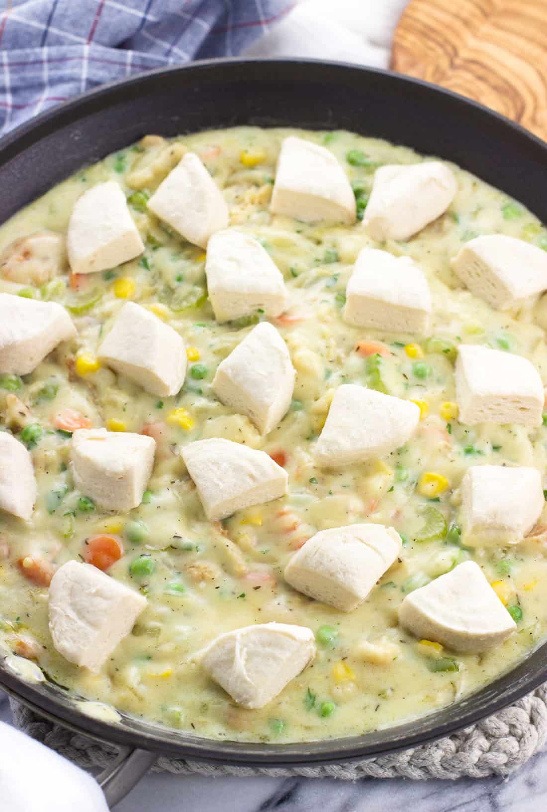 Raw biscuit dough dotted on top of the skillet fish pot pie before baking