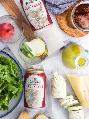 Beer, salad and dressing, compound butter and bread, and fruit ice cubes on a table.