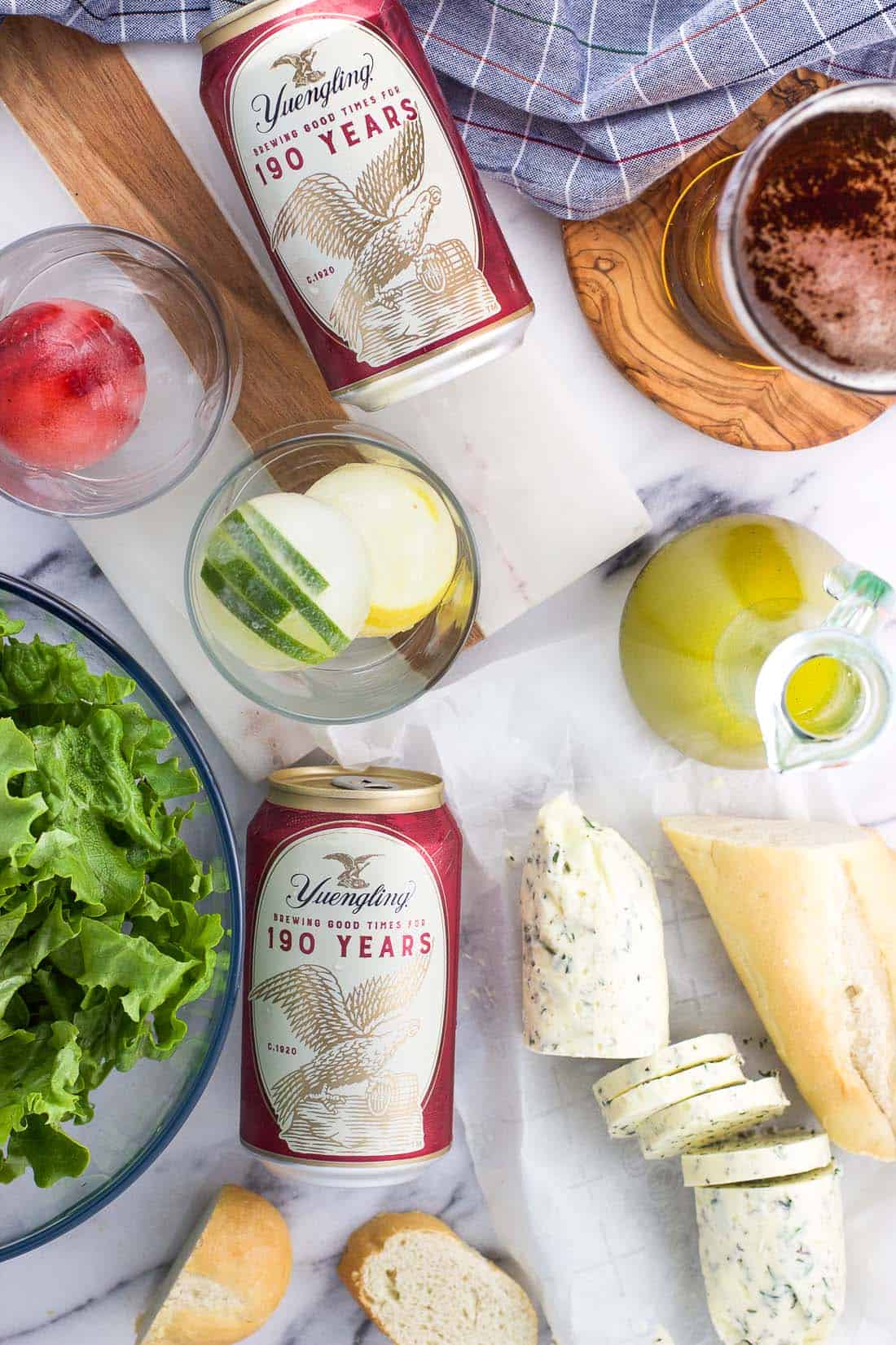 Beer, salad and dressing, compound butter and bread, and fruit ice cubes on a table.