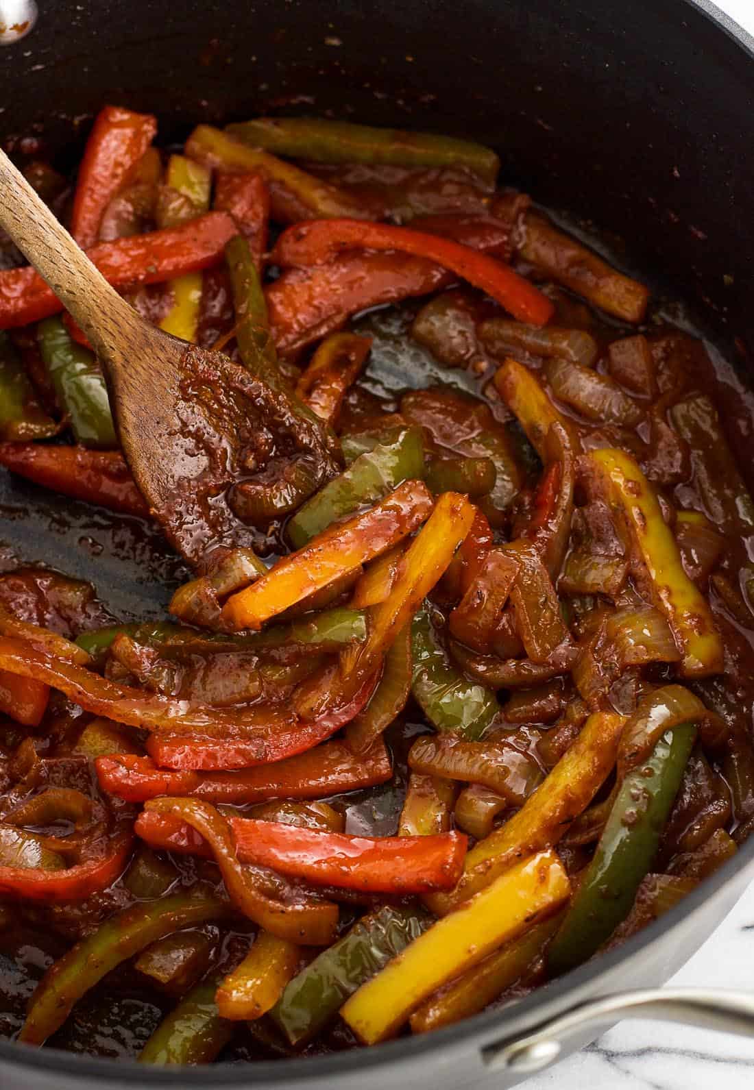 Sliced peppers and onions in a skillet with a thick tomato sauce.