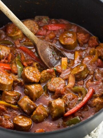 Italian sausage and peppers in sauce in a skillet with a wooden spoon