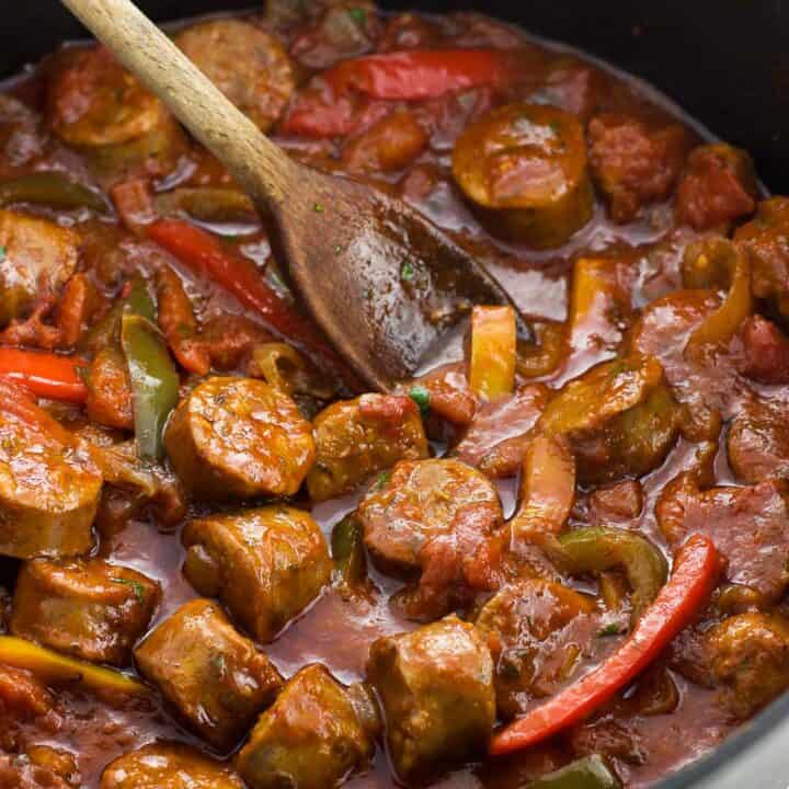 Italian sausage and peppers in sauce in a skillet with a wooden spoon