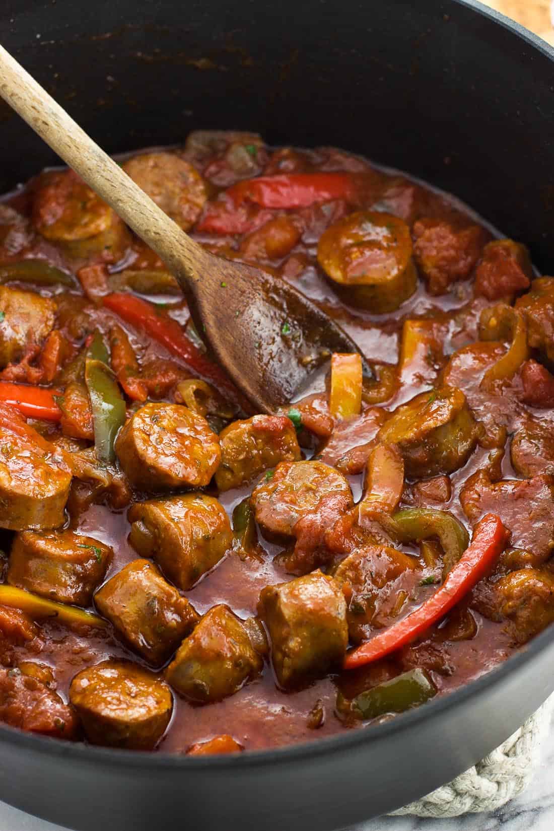 Italian sausage and peppers in sauce in a skillet with a wooden spoon