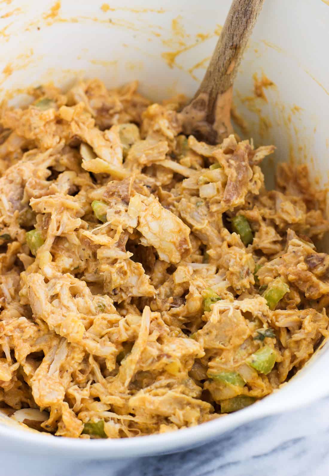 Mixed together buffalo chicken salad in a bowl with a wooden spoon.