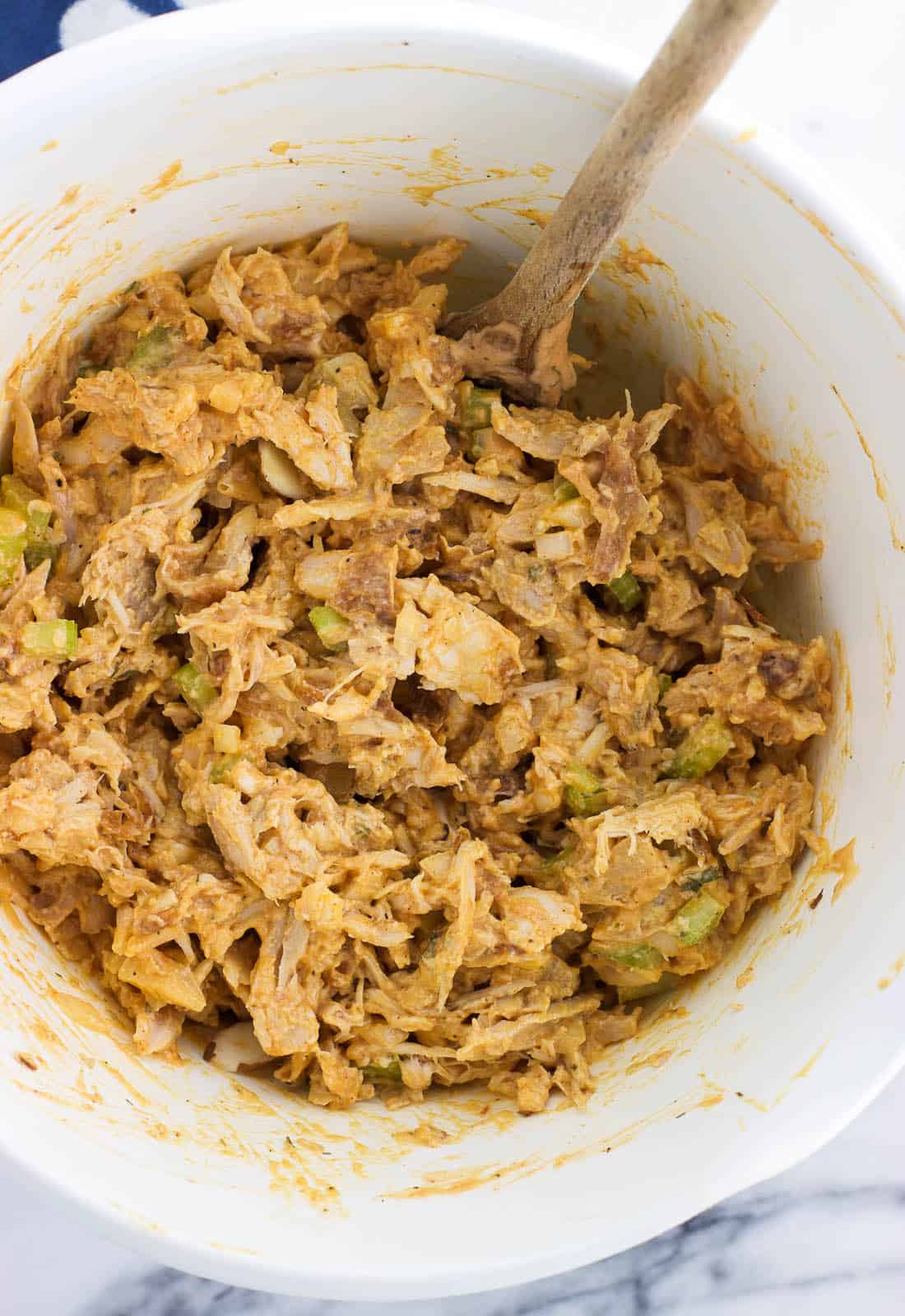 An overhead shot of chicken salad in a mixing bowl with a wooden spoon