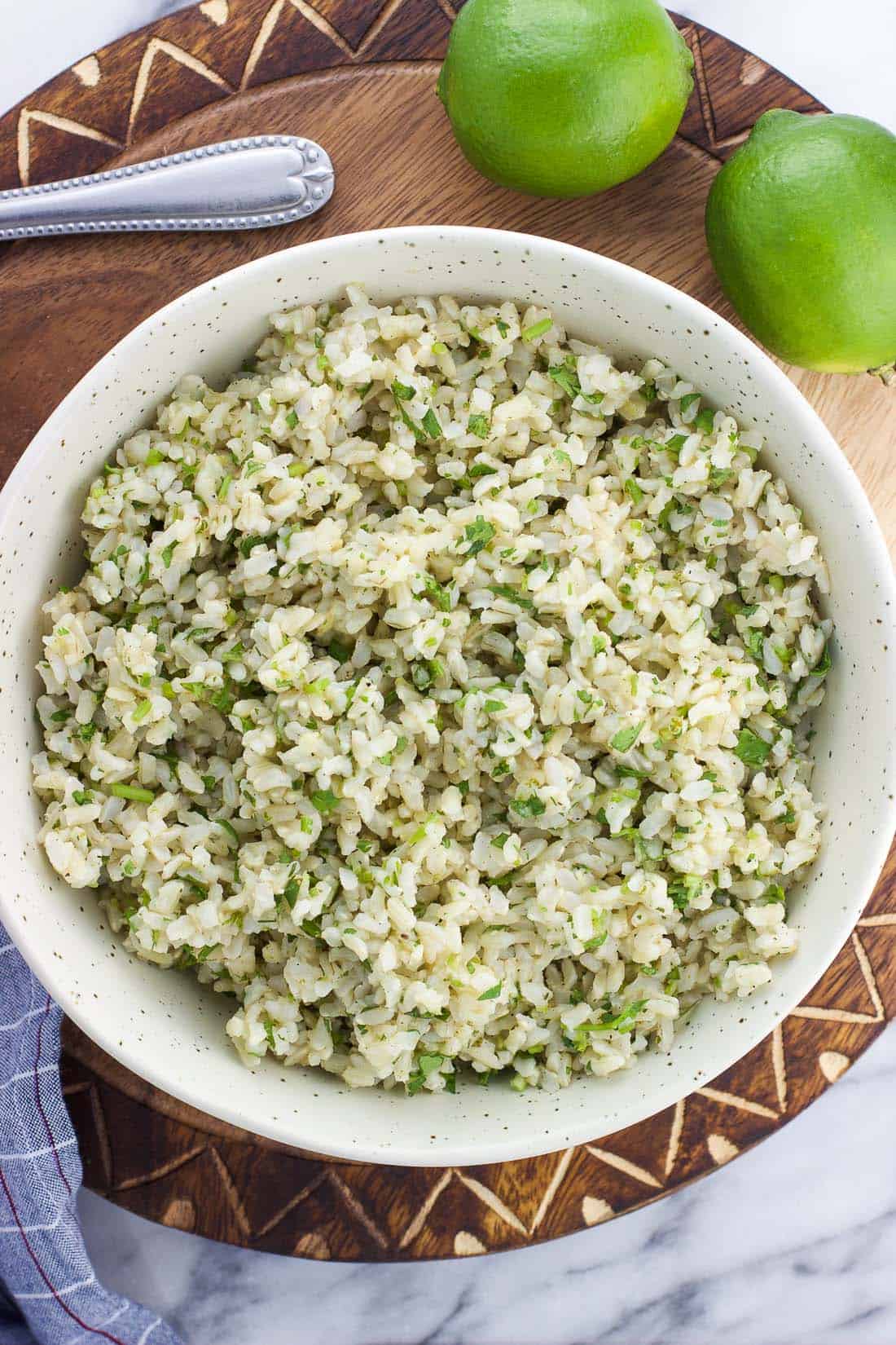 An overhead shot of the cooked and seasoned brown rice in a bowl next to limes.