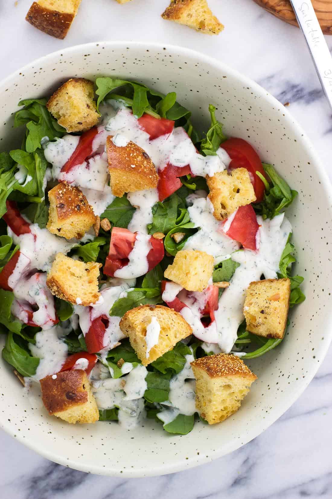 An overhead shot of homemade croutons in a salad with lettuce, tomatoes, and ranch salad dressing.