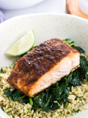 A cooked salmon fillet served on a bed of sauteed spinach over rice