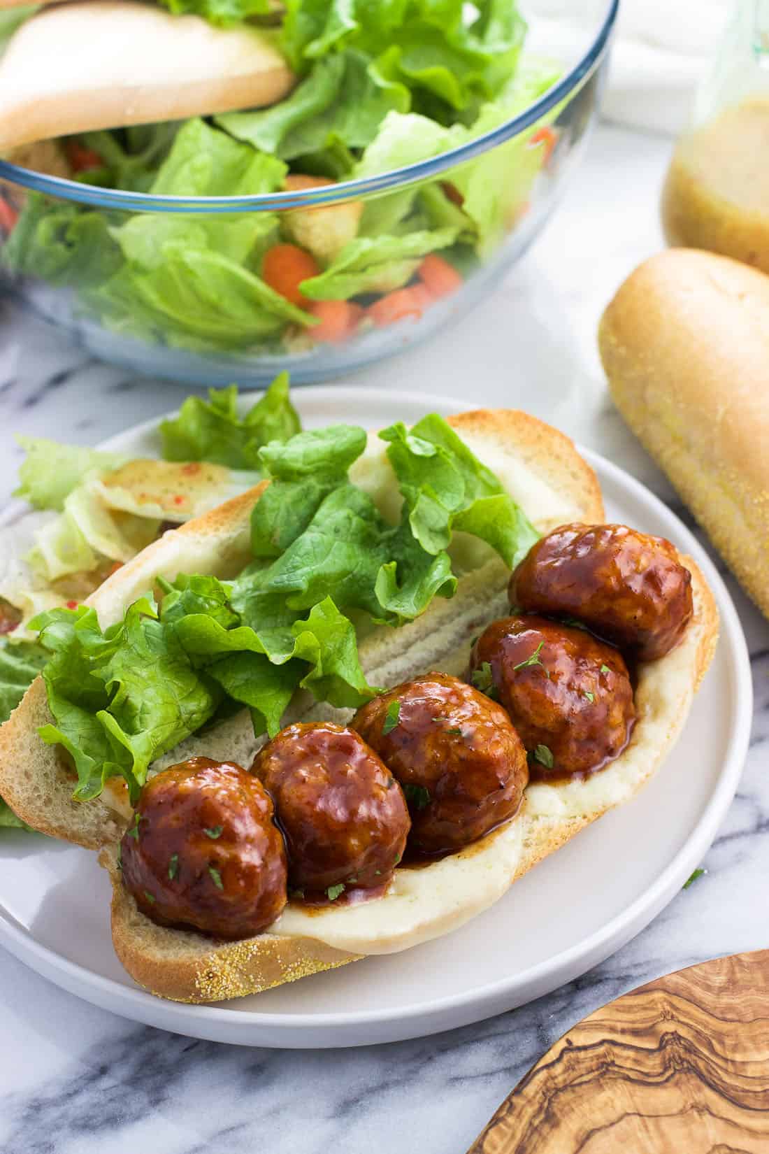 A baked honey BBQ chicken meatball sandwich with cheese and lettuce on a plate.