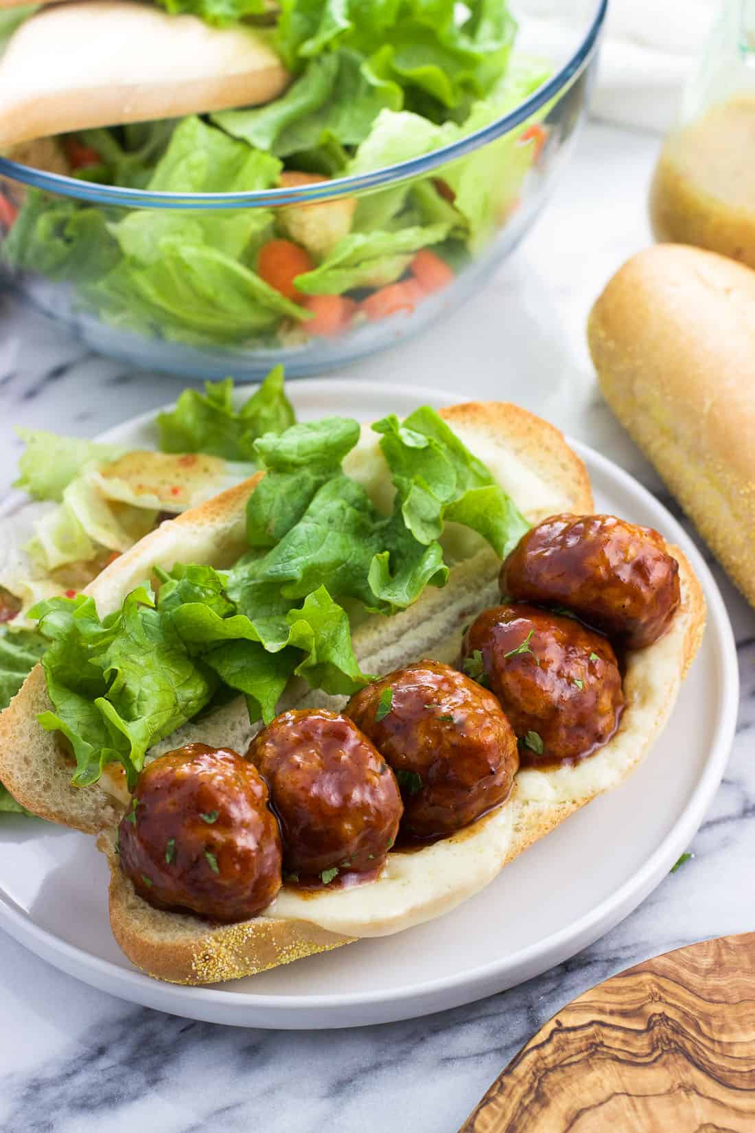 A baked honey BBQ chicken meatball sandwich with cheese and lettuce on a plate