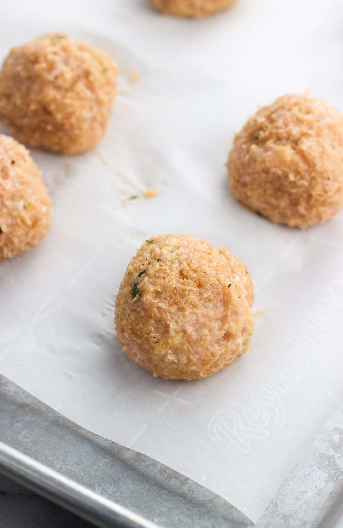 Chicken meatballs on a parchment-lined baking sheet before going into the oven.