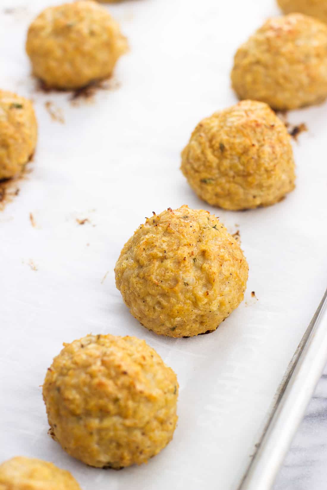 Cooked BBQ chicken meatballs lined up on a parchment-lined baking sheet.